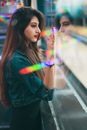 Side view of focused ethnic female standing near glass wall and observing bowling alley while spending time in modern amusement center on blurred background