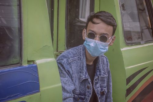 Free Man wearing sunglasses and denim jacket, sitting in green bus, using face mask for protection. Stock Photo