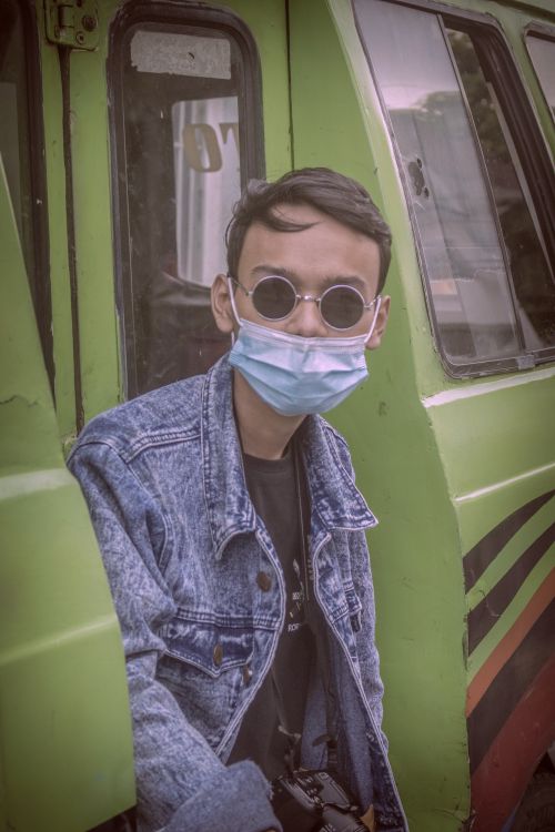 Free A young man wearing a face mask and denim jacket looks at the camera on public transportation. Stock Photo