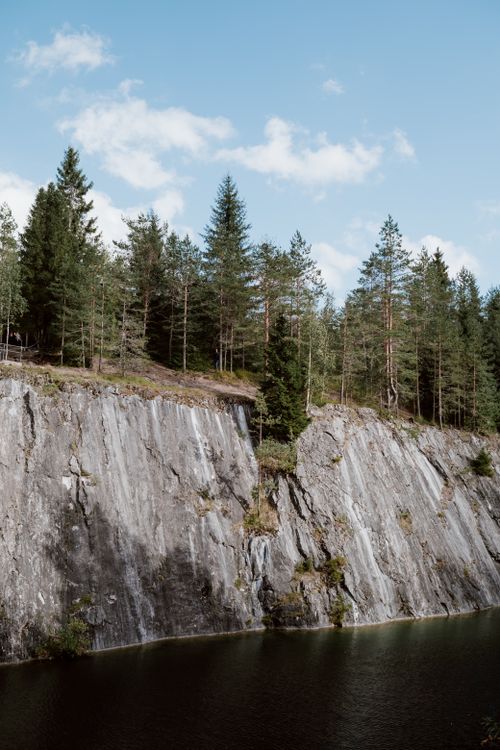 Free Breathtaking view of a rocky riverbank with lush forest trees under a clear blue sky. Stock Photo