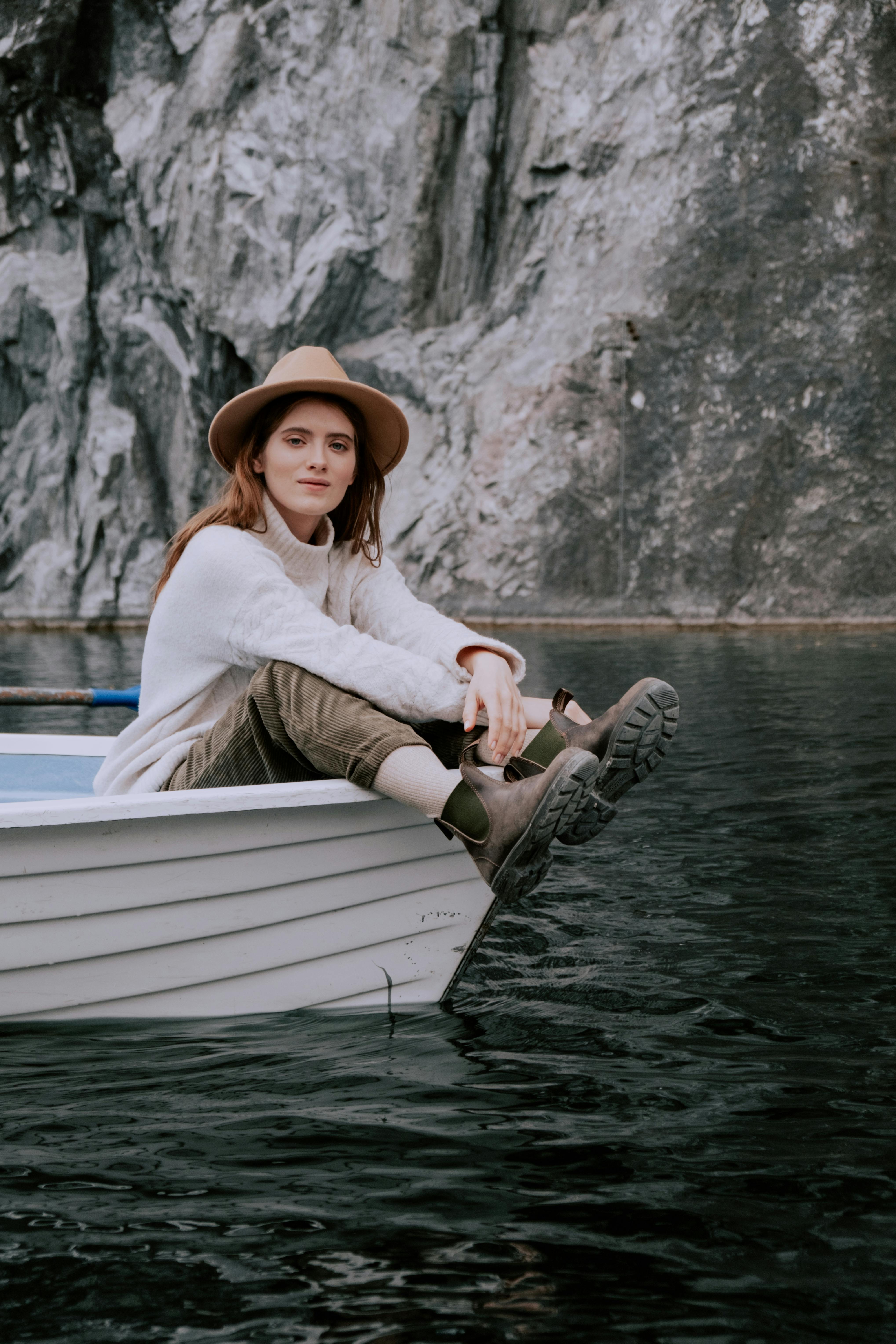 A woman in a hat sits leisurely on a boat by a rocky landscape, enjoying nature's beauty.