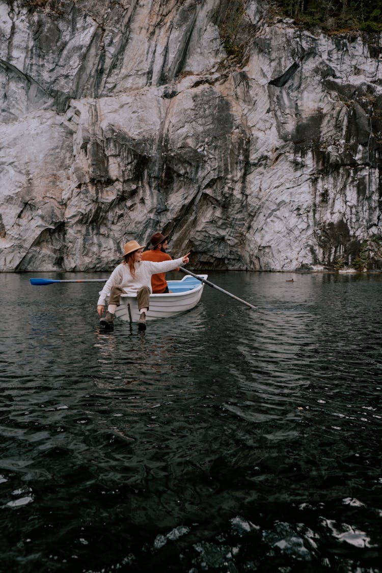 A Man And Woman Sitting On The Boat Near The Rock Formation