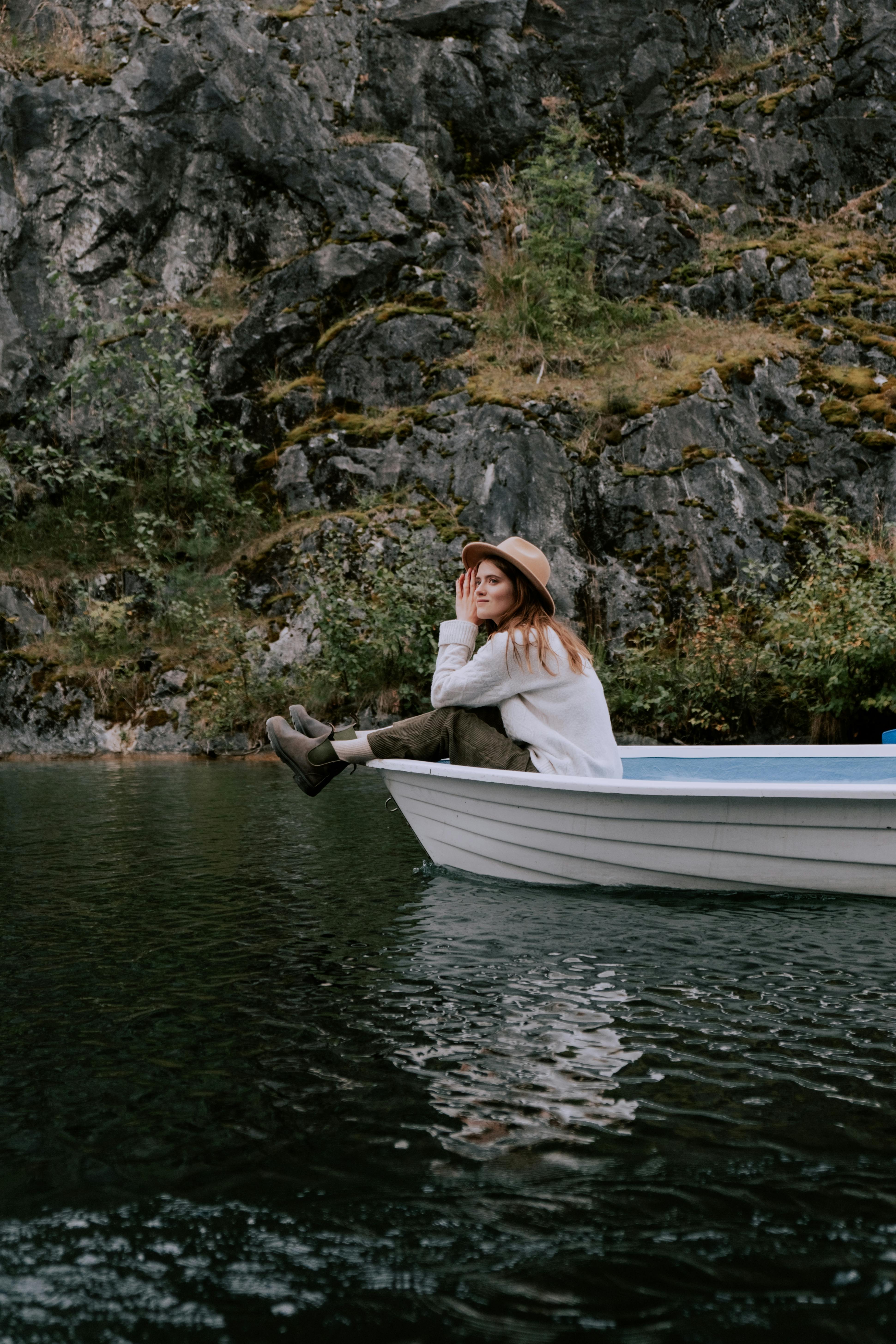 戴帽子的年轻女子坐在船上，在岩石环绕的环境中享受平静的湖面