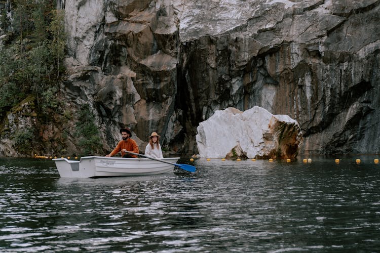 A Man And Woman Sitting On The Boat Near The Rock Formation