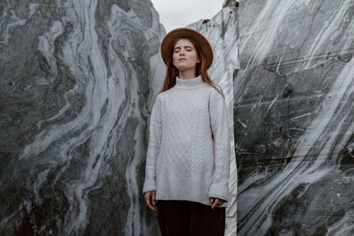 Woman in White Sweater and Black Pants Standing Beside Gray Marble Wall