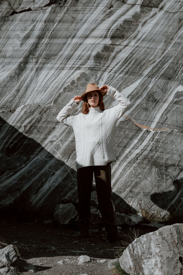 Woman In White Sweater And Black Pants Standing Beside  Rock Formation