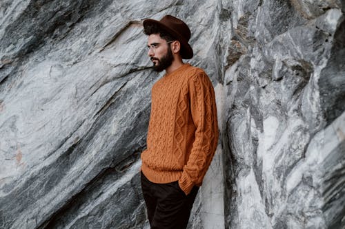 Man in a Brown Sweater is Standing Beside Gray Rock Formation