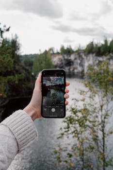 A person capturing a scenic view of a river and forest with a smartphone.