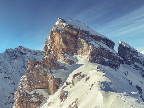 Severe landscape of rocky rough mountain peaks with sharp stiff slopes covered with snow under blue sky on sunny winter day