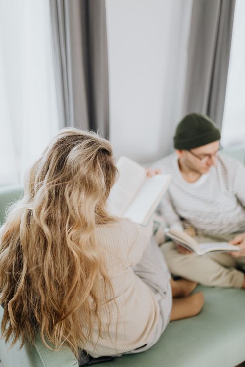 Free A young couple enjoying a quiet reading moment on a couch in a well-lit room. Stock Photo