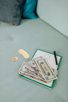 A close-up of US dollar bills and cryptocurrency coins on a notebook with a pen.