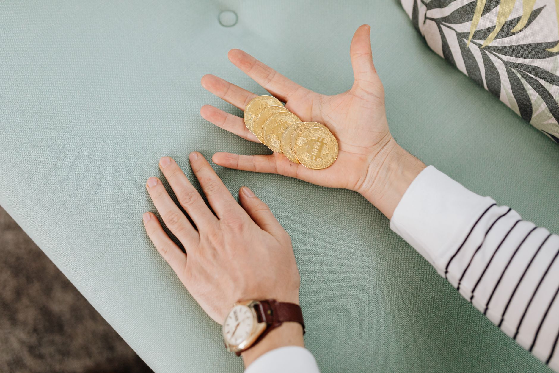 Close-up of hands holding bitcoins on a pastel-colored sofa, showcasing modern finance.