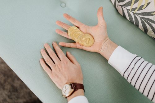 Free Close-up of hands holding bitcoins on a pastel-colored sofa, showcasing modern finance. Stock Photo