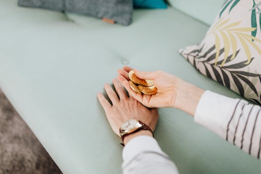 Close-up of hands holding gold coins on a sofa with decorative pillows.