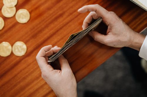 Free Close-up of hands counting currency with coins scattered on a wooden table. Perfect for finance and business themes. Stock Photo