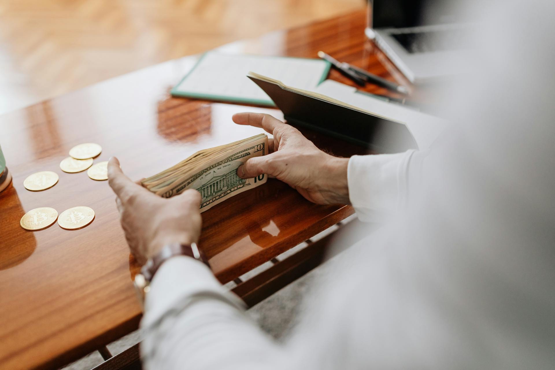 Person counting cash and coins on a wooden table, emphasizing financial tasks.