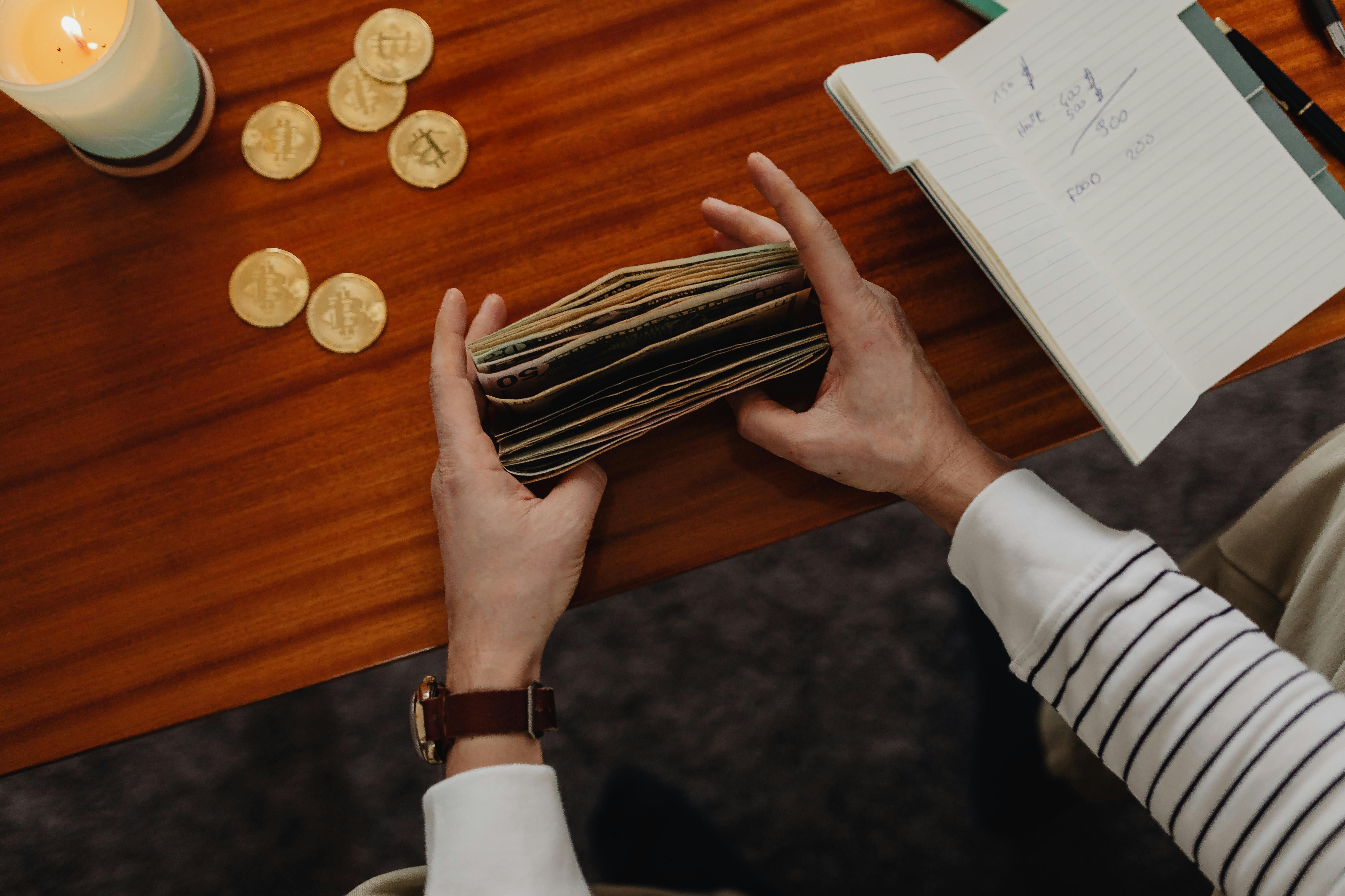 person counting bills and bitcoins on table