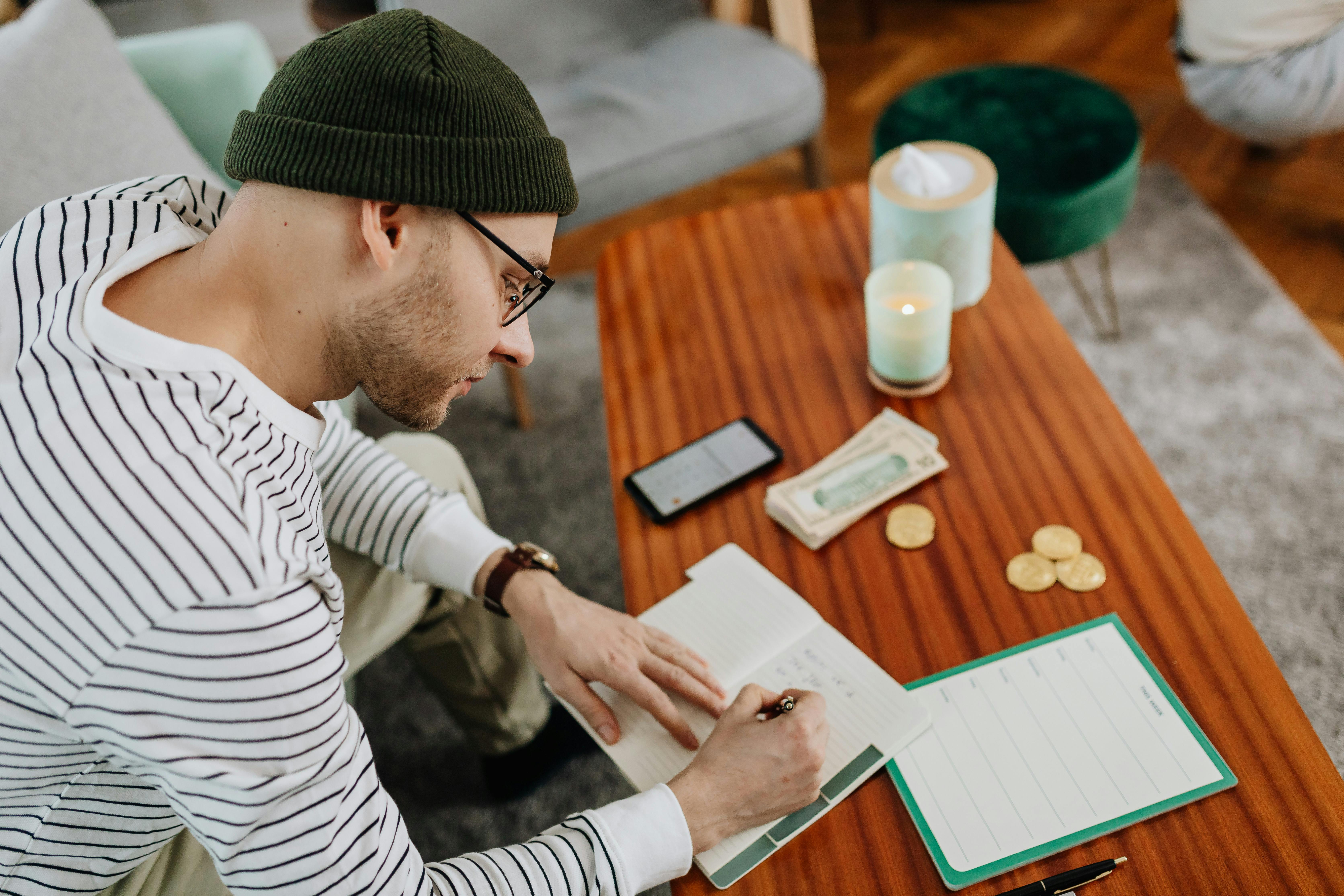 Adult man writing notes at a wooden table with a notebook and accessories.