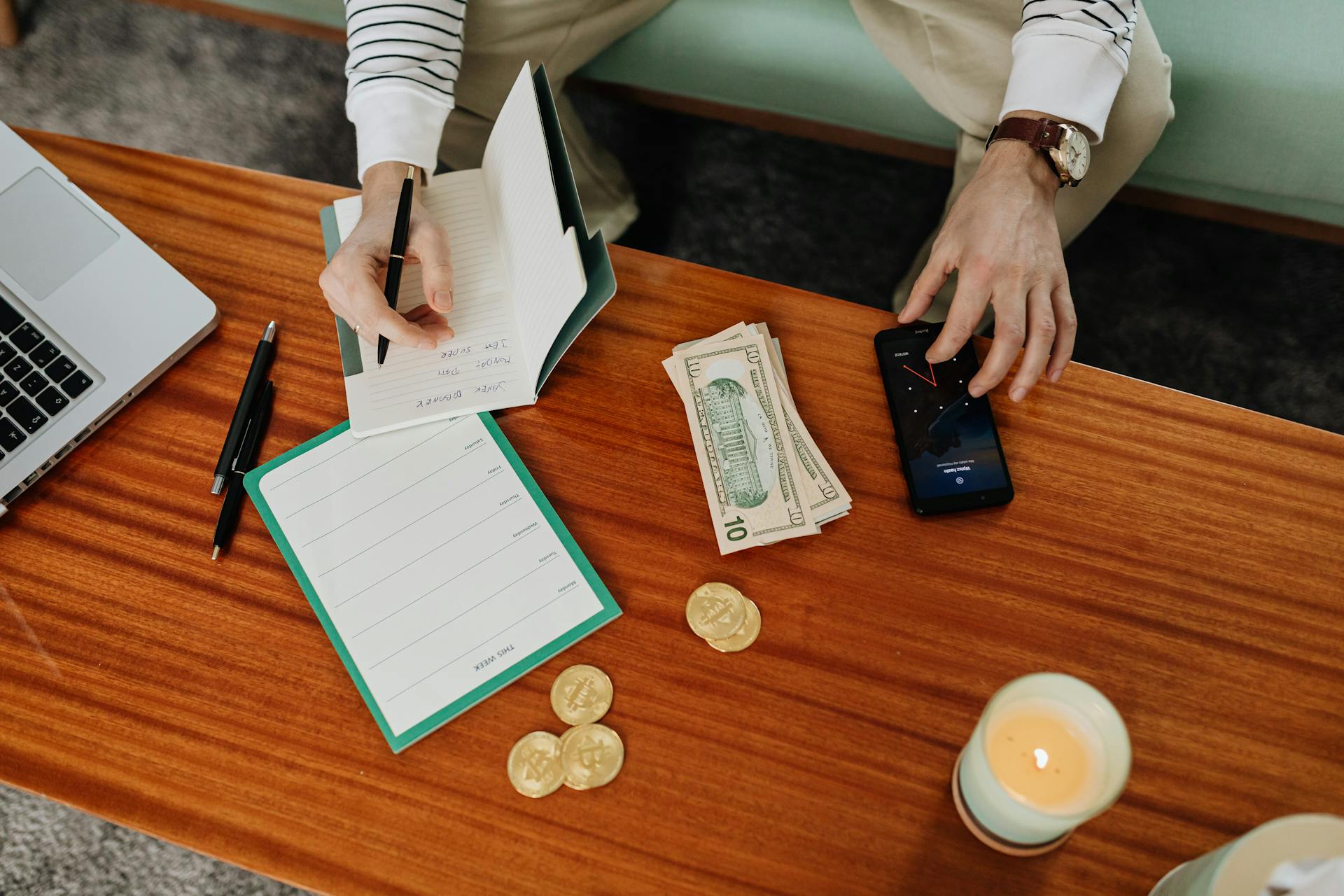 Person organizing finances with a notebook and smartphone on a wooden table.