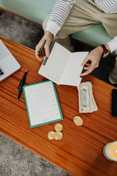 Person organizing budget with notebook and cash on a wooden table, perfect financial planning concept.