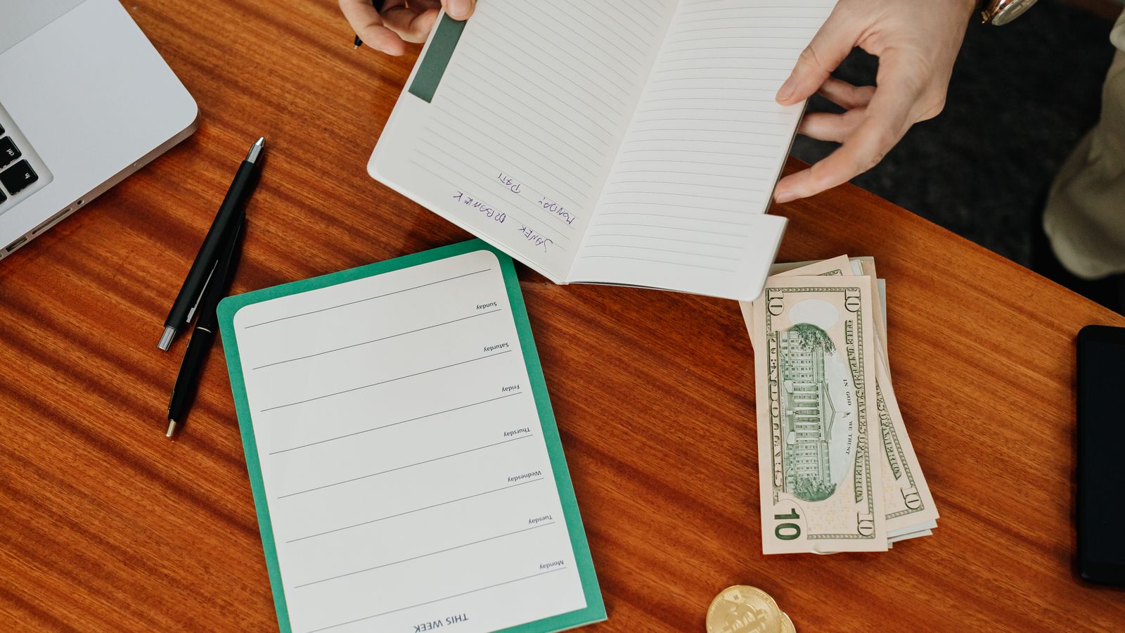 Hands organising a budget with a notebook and cash on a wooden table