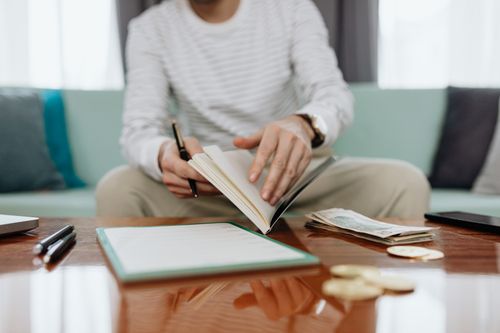Free Individual reviewing finances at a table with notebook, money, and laptop. Stock Photo