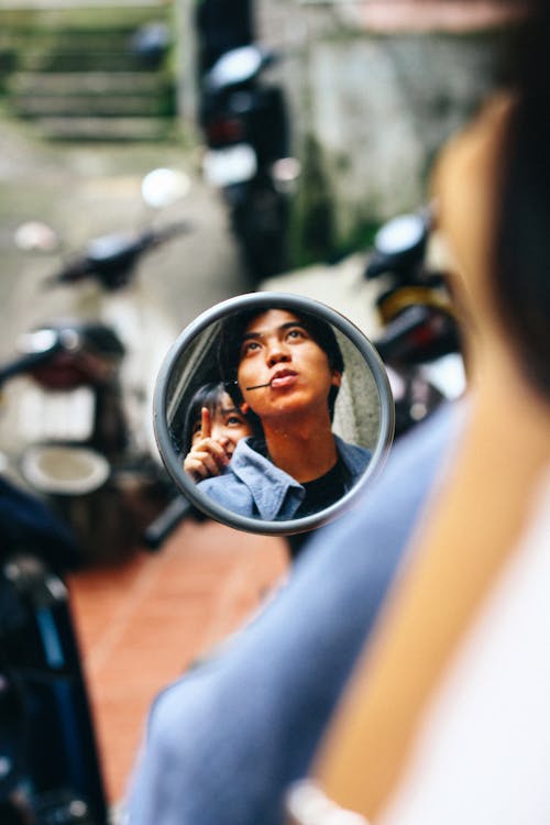 Reflection of young ethnic couple sitting on motorcycle while pointing and looking away