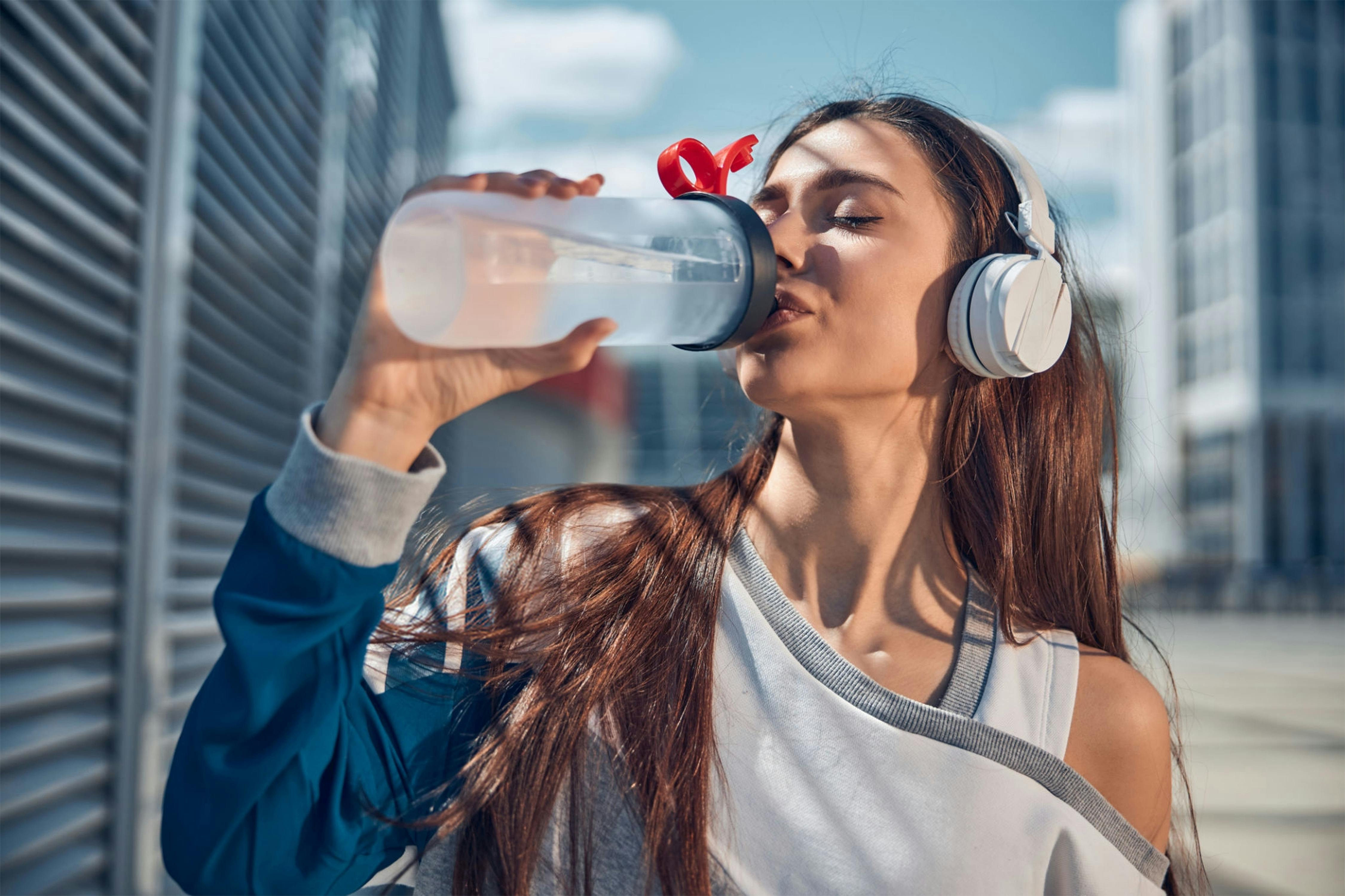 Free A Woman Wearing Headphones and Drinking Water Stock Photo