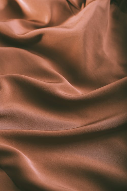 From above of elegant brown draped silk fabric with smooth texture as abstract background