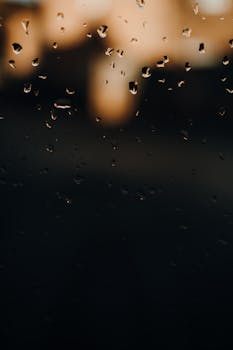 Blurred raindrops on a window with soft evening lights, creating a dreamy atmosphere.