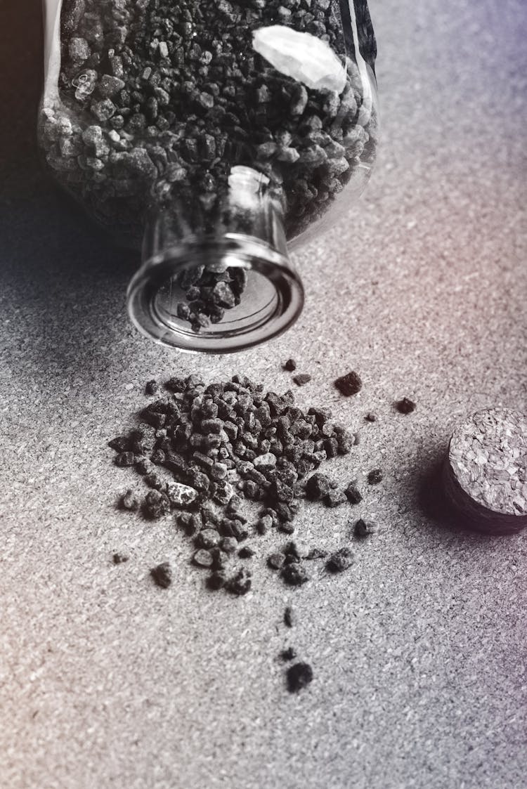 Glass Bottle With Activated Charcoal Granules Scattered On Table