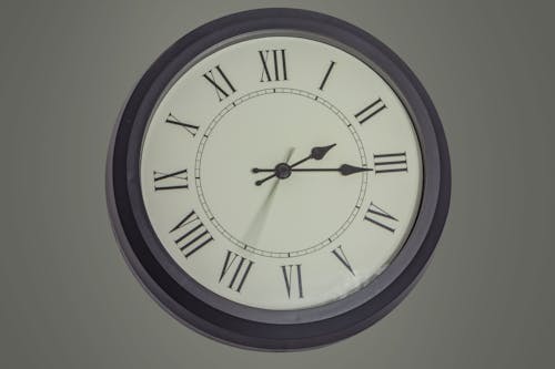 Round black mechanical clock with Roman numerals hanging on gray wall