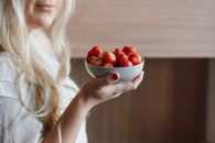 Anonymous woman showing bowl of ripe fresh strawberries at home