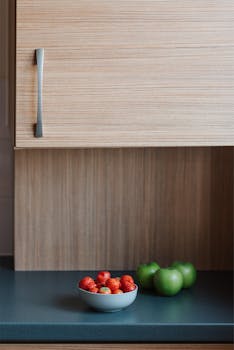 Bowl of fresh ripe appetizing strawberries placed on counter near green apples in kitchen in sunny morning