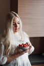 Pensive young blondie eating fresh strawberries in kitchen