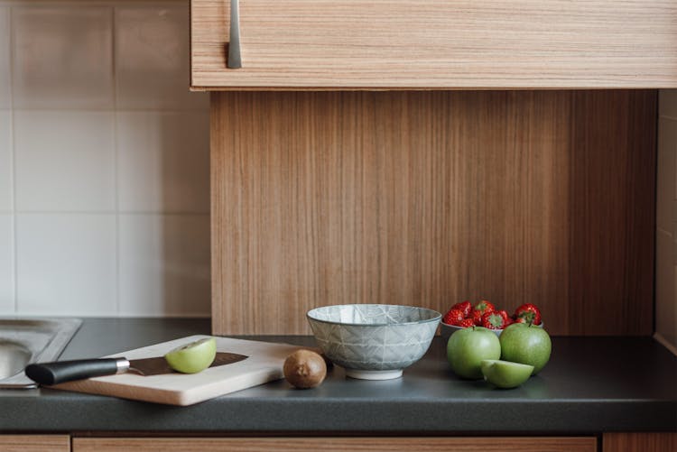 Assorted Fresh Fruits Placed On Counter With Bowl And Cutting Board