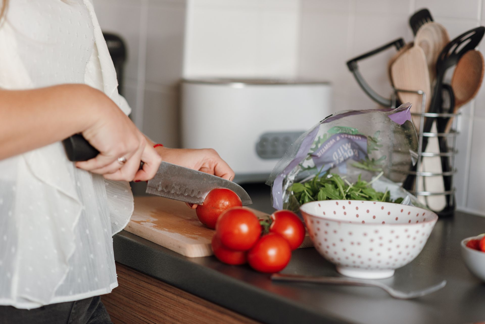 Crop anonymous housewife in casual clothes cutting fresh ripe tomatoes with sharp knife on wooden cutting board while cooking in kitchen