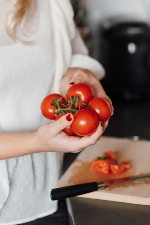 Free Crop unrecognizable housewife with bunch of fresh ripe tomatoes and sharp knife while cooking in kitchen Stock Photo