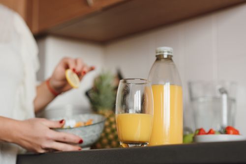 Free Crop unrecognizable female standing near table with fresh orange juice while cooking fruit salad in kitchen Stock Photo