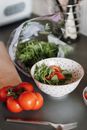 From above of cut fresh ripe tomatoes with greenery in bowl on table in kitchen