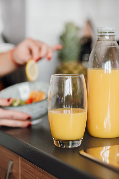 Free Glass and plastic bottle with natural fruit juice on table near bowl with salad against crop blurred lady having meal Stock Photo