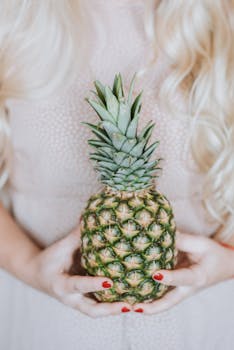 Unrecognizable female with long blond hair holding big fresh pine apple in hands
