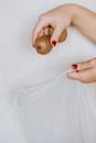 Unrecognizable female putting small kiwi fruit in reusable zero waste sack on grey background