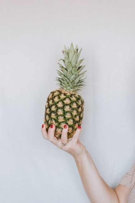 Unrecognizable female holding in hand big heavy ripe pineapple on light grey background