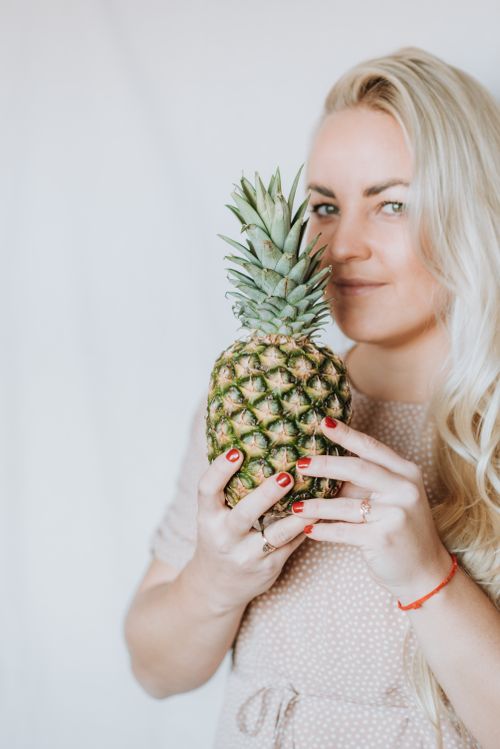 Free Young positive blond female smelling aroma of fresh pineapple and looking at camera Stock Photo
