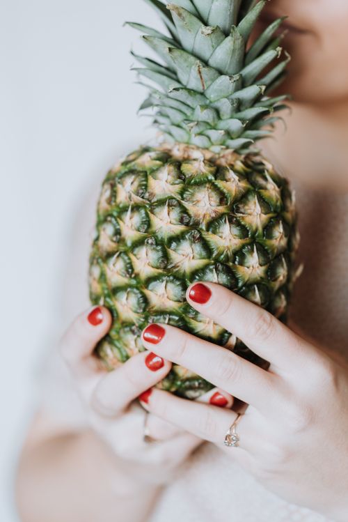 Free Unrecognizable woman holding in hands big pineapple and enjoying fresh aroma on grey background Stock Photo