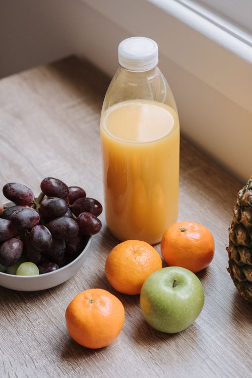 Free High angle of plastic bottle with juice bowl with red grapes and some mandarins and green apple on table Stock Photo