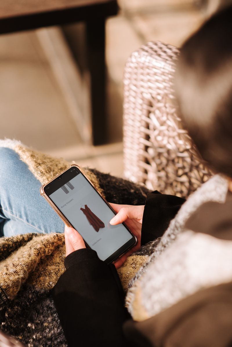 A woman browsing a shopping app on her smartphone while relaxing at home