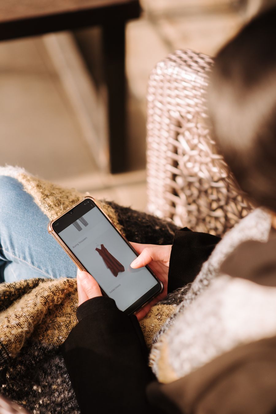 A woman browsing a shopping app on her smartphone while relaxing at home