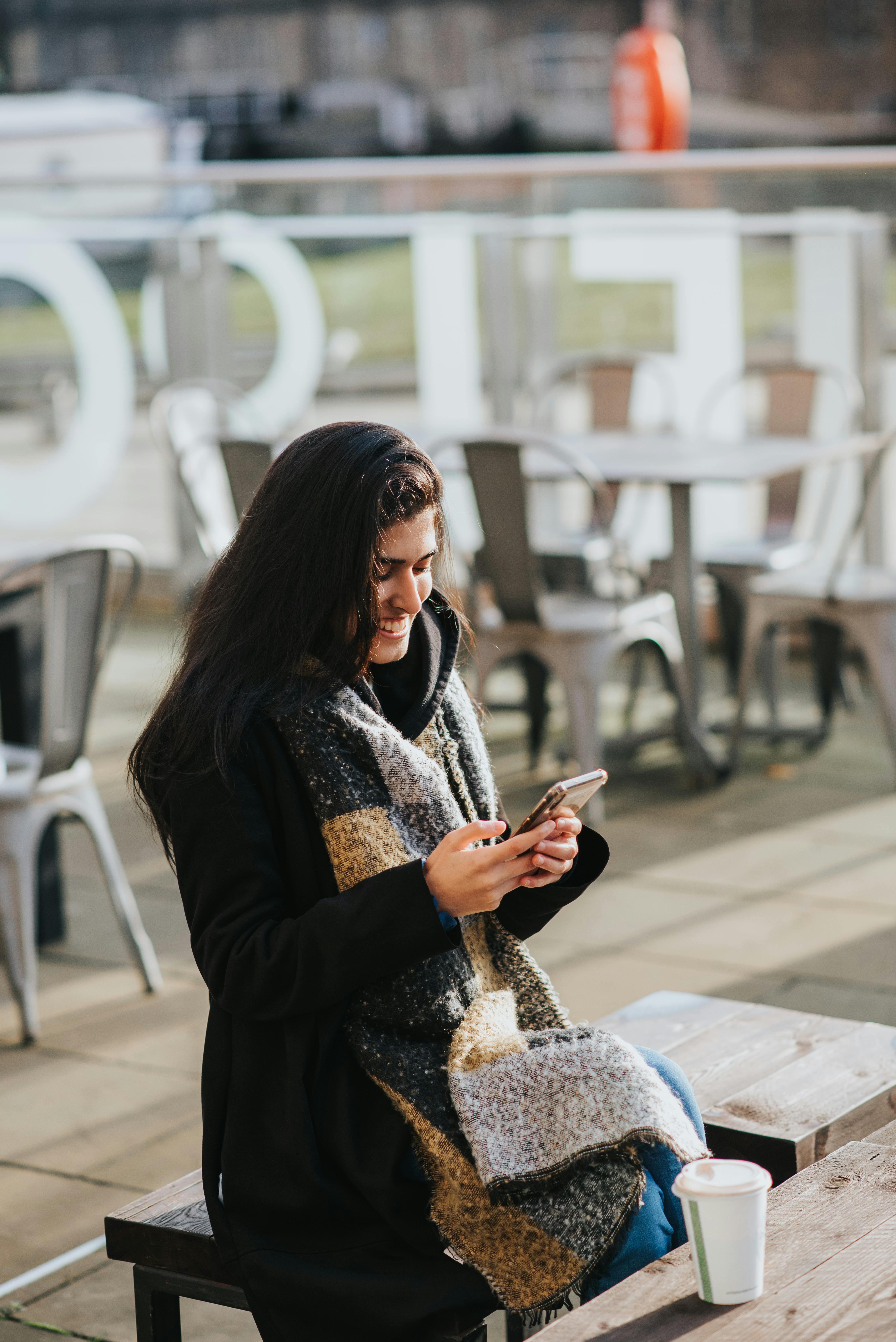 smiling ethnic woman chatting on smartphone in street cafeteria